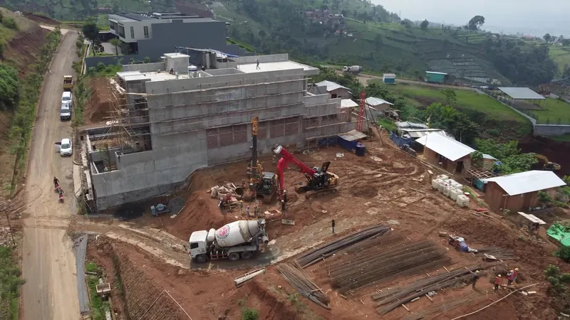 Dinding penahan menerus mengelilingi galian di lahan berkontur, dengan rig bor di dalamnya